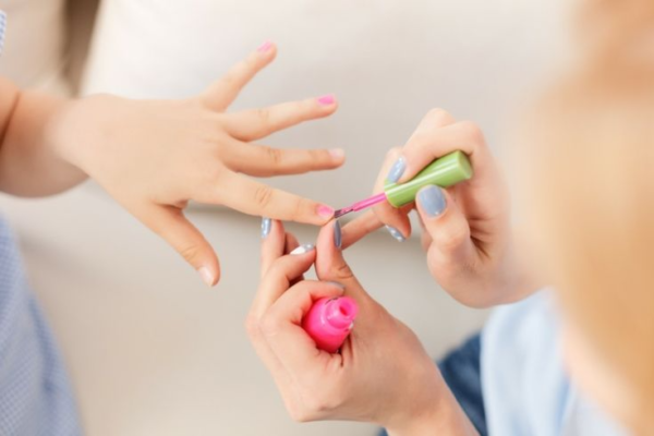 Una especialista aplicando pintura de uñas a una niña cuidadosamente
