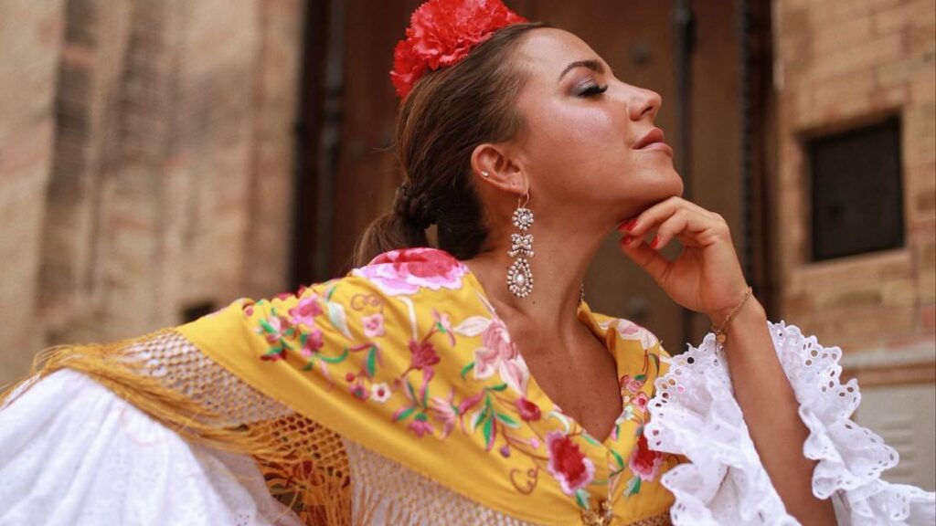 Una mujer utilizando un traje de ceremonia elegante mientras que acaricia su barbilla con sus dedos para exhibir sus uñas pintadas