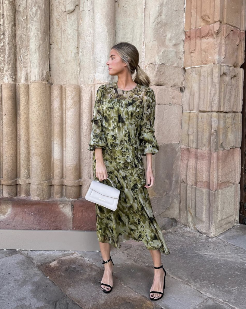 Una mujer posando con un elegante vestido y una cartera blanca