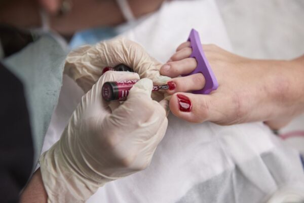 Un especialista haciendo un tratamiento de pedicura pintandole las uñas a una mujer